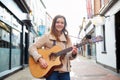 Portrait Of Young Female Musician Busking Playing Acoustic Guitar And Singing Outdoors In Street