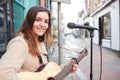 Portrait Of Young Female Musician Busking Playing Acoustic Guitar And Singing Outdoors In Street Royalty Free Stock Photo