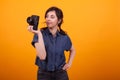 Portrait of young female photographer holding her camera in studio over yellow background Royalty Free Stock Photo
