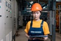 Portrait of a young female worker in uniform and helmet with a folder in her hand, standing near the gauges. Factory equipment is Royalty Free Stock Photo