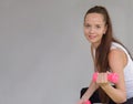 Portrait of young fitness sporty woman in sportswear sitting on fit ball and exercise with dumbbell on gray colour background. Royalty Free Stock Photo