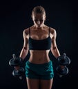 Portrait of a young fitness woman in sportswear doing workout with dumbbells on black background. Tanned athletic girl. Royalty Free Stock Photo