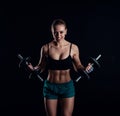 Portrait of a young fitness woman in sportswear doing workout with dumbbells on black background. Tanned athletic girl. Royalty Free Stock Photo