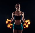 Portrait of a young fitness woman in sportswear doing workout with fiery dumbbells on black background. Tanned athletic girl.