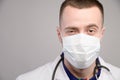 Portrait of a young friendly friendly Caucasian doctor in a protective medical mask on a gray background. A man winks