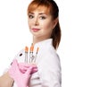 Young beautiful red-haired woman doctor or nurse in white medical uniform and gloves holds shows five syringes