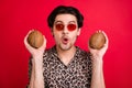 Portrait of young funky good mood amazed man in sunglass hold two coconuts tropical fruit isolated on red color