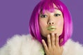 Portrait of young funky woman in pink wig blowing kiss over purple background Royalty Free Stock Photo