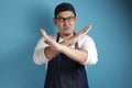 Portrait of young funny angry male Asian chef or waiter shows crossed arms gesture, giving warn to stop Royalty Free Stock Photo