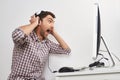 Portrait of young funny bearded male gamer in checkered shirt playing games on personal computer, wearing headphones Royalty Free Stock Photo