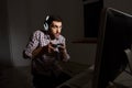 Portrait of young funny bearded man in headphones wearing checked shirt playing computer games on personal computer with Royalty Free Stock Photo