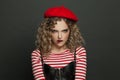 Portrait of young funny woman in red french style beret scowling on black wall background