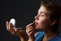 Portrait of a young girl on a black background that paints her lips with red lipstick. Royalty Free Stock Photo