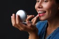 Portrait of a young girl on a black background that paints her lips with red lipstick. Royalty Free Stock Photo