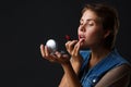 Portrait of a young girl on a black background that paints her lips with red lipstick. Royalty Free Stock Photo