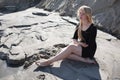 Portrait of young girl in black dress with long blonde hair sitting on beach Royalty Free Stock Photo