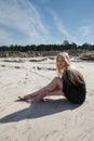 Portrait of young girl in black dress with long blonde hair sitting on beach Royalty Free Stock Photo