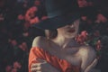 Portrait of a young girl in a black hat, and evening gown, against the background of red rose flowers. In a warm artistic tint Royalty Free Stock Photo