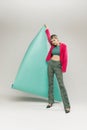 Portrait of young girl in bright jacket and vintage pants posing with paper piece isolated over grey studio background Royalty Free Stock Photo