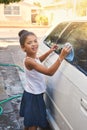 Portrait, young girl and car in driveway with water for cleaning, soap and cloth outdoors at home. Happy kid, washing Royalty Free Stock Photo