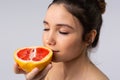 Portrait of a young girl with closed eyes enjoying the aroma of fresh, juicy grapefruit on a gray background. Enlarged