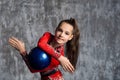 A portrait of young girl gymnast in a red suit makes exercise with a ball against a gray wall. She holds the ball between her hand Royalty Free Stock Photo