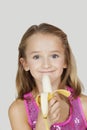 Portrait of young girl holding banana against gray background