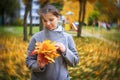 Portrait of young girl holding bouquet of fallen autumn yellow leaves in an autumn park with swirling bokeh on the background Royalty Free Stock Photo