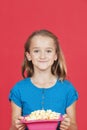 Portrait of young girl holding popcorn container against red background Royalty Free Stock Photo
