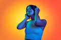 Portrait of young girl listening to music in headphoes isolated over orange background in neon light. Satisfaction