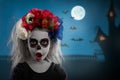 Portrait of a young girl in a make-up on a Halloween wreath with red flowers on her head. Royalty Free Stock Photo