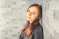 Portrait of a young girl without makeup on her face in a black jacket against a gray brick wall. Royalty Free Stock Photo