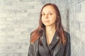 Portrait of a young girl without makeup on her face in a black jacket against a gray brick wall. Royalty Free Stock Photo