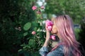 Portrait of young girl with pink hair sniffing rose flower.