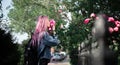 Portrait of young girl with pink hair sniffing rose flower.