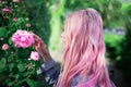 Portrait of young girl with pink hair sniffing rose flower.