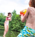 Young girl playing squirt guns with her brother on pier during summer Royalty Free Stock Photo