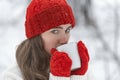 Portrait of young girl in red hat and mittens in snowy park. Beautiful young woman drink hot beverage from cup in winter outdoor Royalty Free Stock Photo