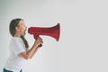 Portrait of young girl shouting using megaphone over background Chil in white shirt, studio shot