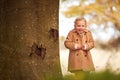 Portrait Of Young Girl Standing By Trunk Of Autumn Tree Playing Hide And Seek In Garden Royalty Free Stock Photo