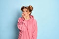 Portrait of young girl, student in pink hoodie posing with stressful expression over blue studio background. Exam time