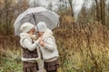 Portrait of young girls - twins, standing under an umbrella in the park, looking at each other, hugging