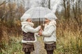 Portrait of young girls - twins, standing under an umbrella in the park, looking at each other, laughing