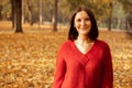 Portrait of young glad wonderful woman standing outside near trees among yellow fallen leaves in forest park, posing. Royalty Free Stock Photo