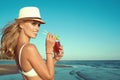 Portrait of young glam smiling blond lady in white swimming bra and panama drinking cocktail through a straw