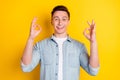 Portrait of young good mood cheerful guy showing okay sign advertisement wear jeans shirt isolated on yellow color Royalty Free Stock Photo