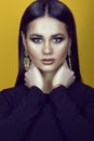 Portrait of young gorgeous blue-eyed dark-haired model with professional make up in golden colors wearing black top and earrings Royalty Free Stock Photo