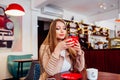 Portrait of young gorgeous female drinking coffee and looking with smile out of the coffee shop window while enjoying her leisure Royalty Free Stock Photo