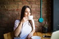 Portrait of young gorgeous female drinking tea and looking with smile out of the coffee shop window while enjoying her leisure tim Royalty Free Stock Photo