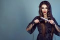 Portrait of young gorgeous model with long hair wearing black silk peignoir holding curling wand and hair straightener crossed